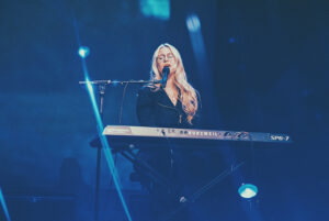 A vibrant female musician performing on stage with a keyboard at the California Strawberry Festival.